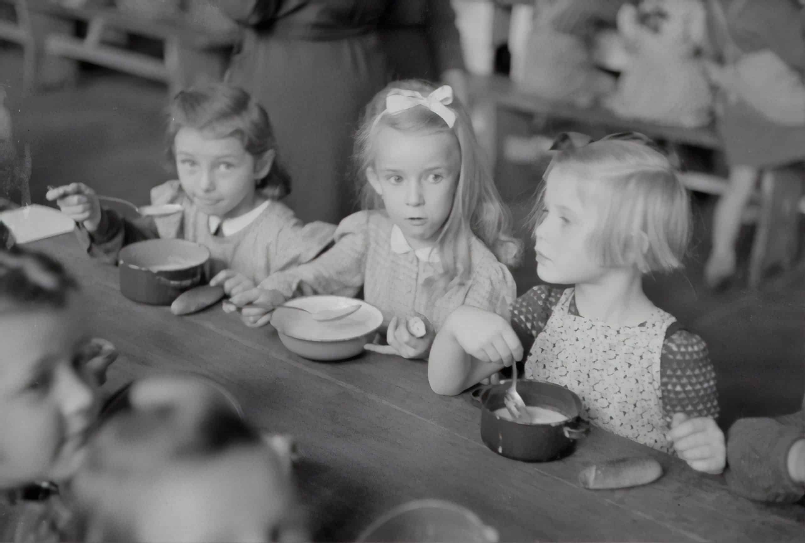 Three young girls at a table eating and are at risk for eating disorders.