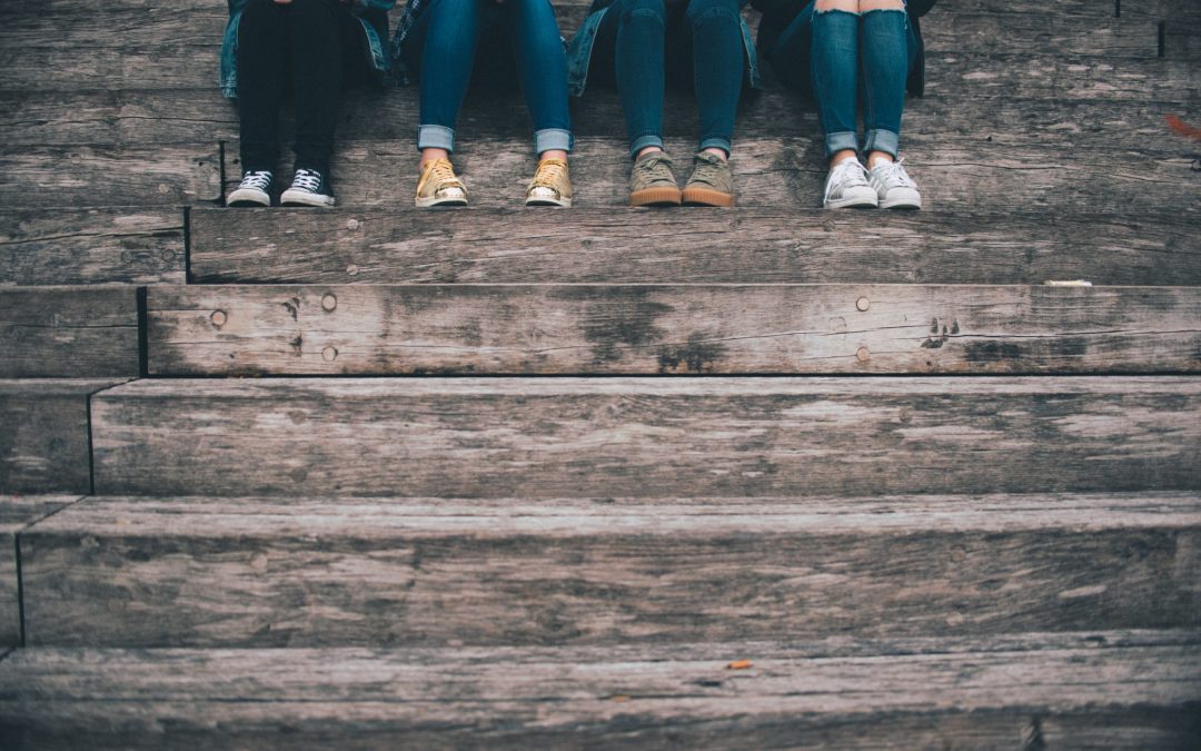 A photo of four girls of the tween years are sitting on a step, with just their legs showing from the knee down. They represent some of the influences on body image at that age.