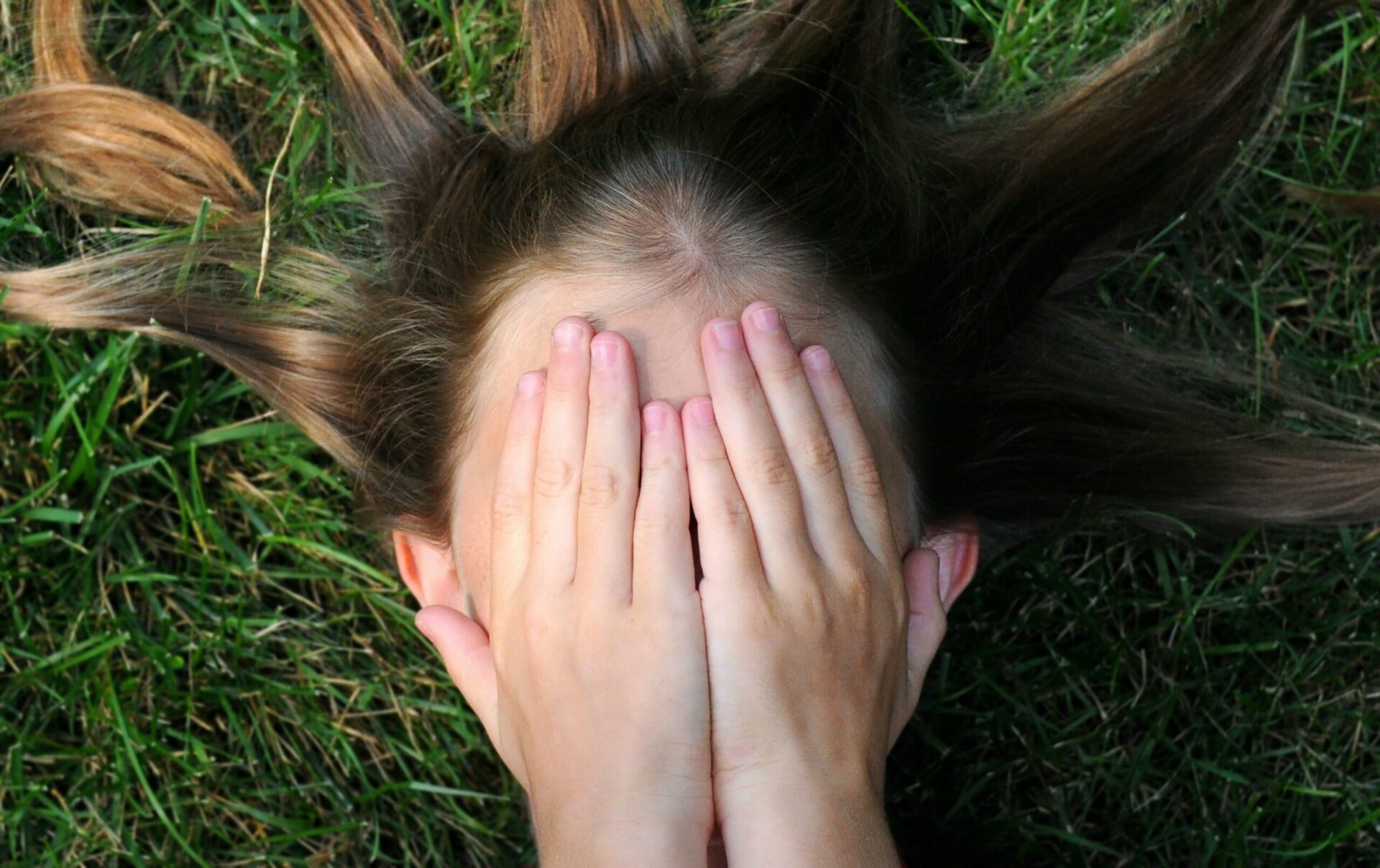 A photo of a girl with her hands covering her face, as she is laying down, representing signs of a eating disorder a parent should identify
