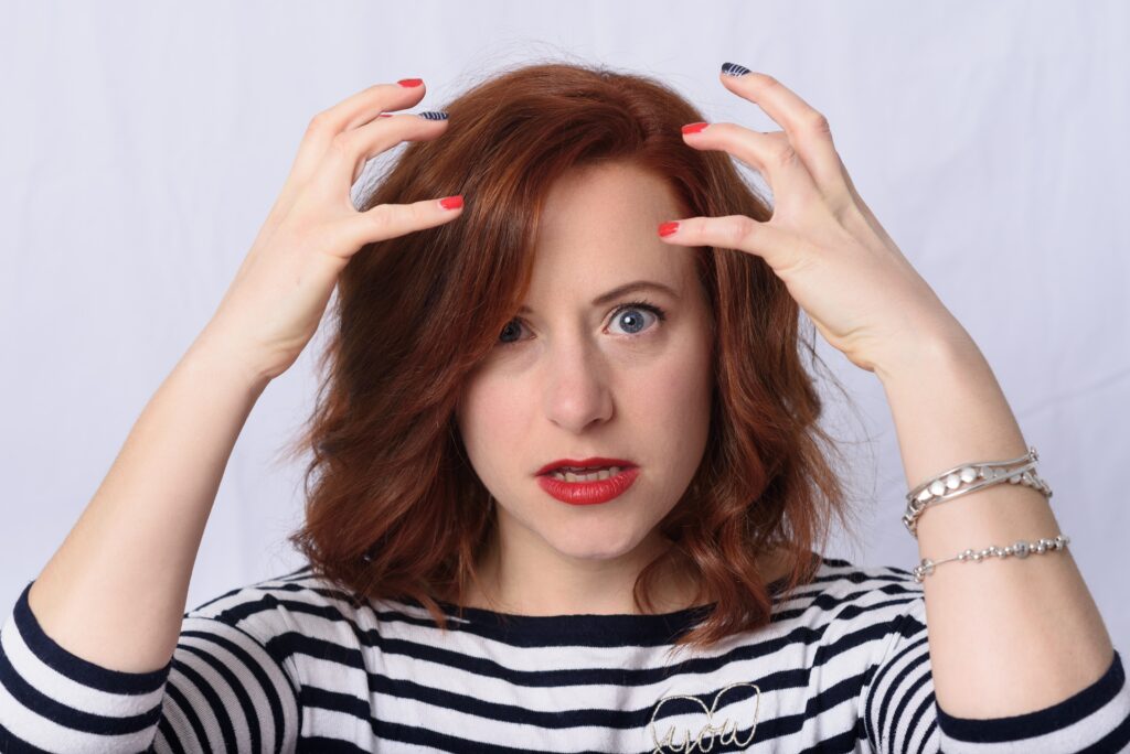 A headshot of a red headed woman with her hands by her head, similar to how a Highly Sensitive Person might gesture