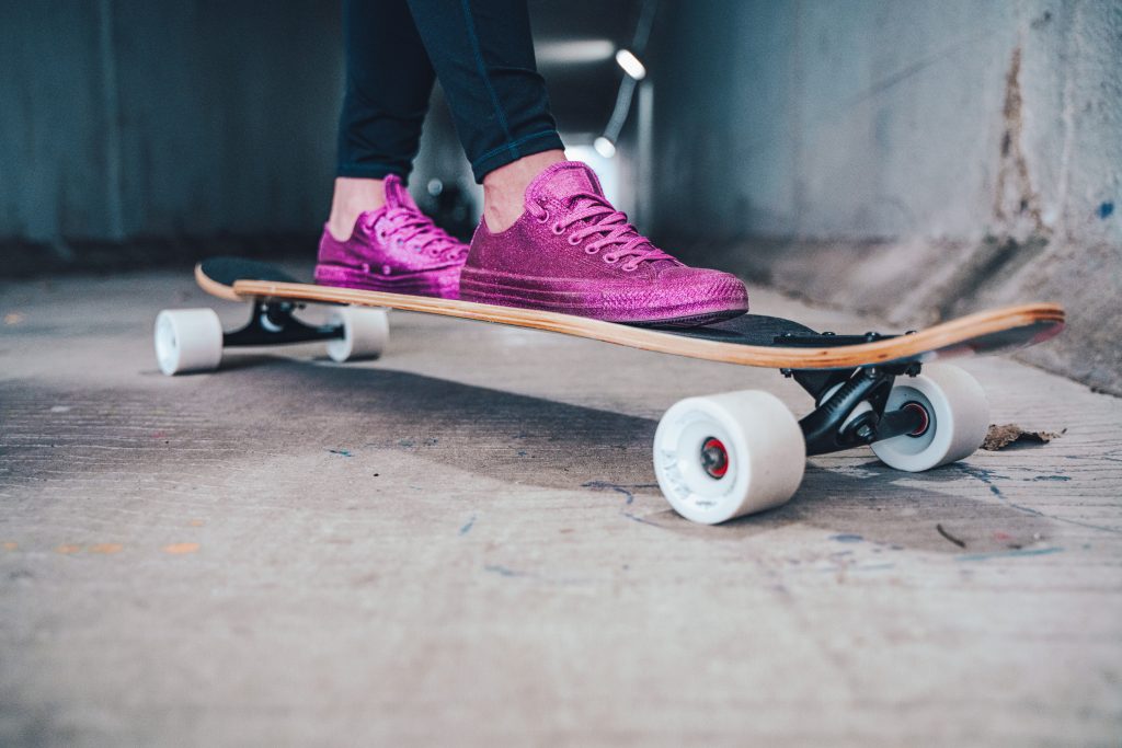 A woman's feet in purple sneakers on a skateboard.